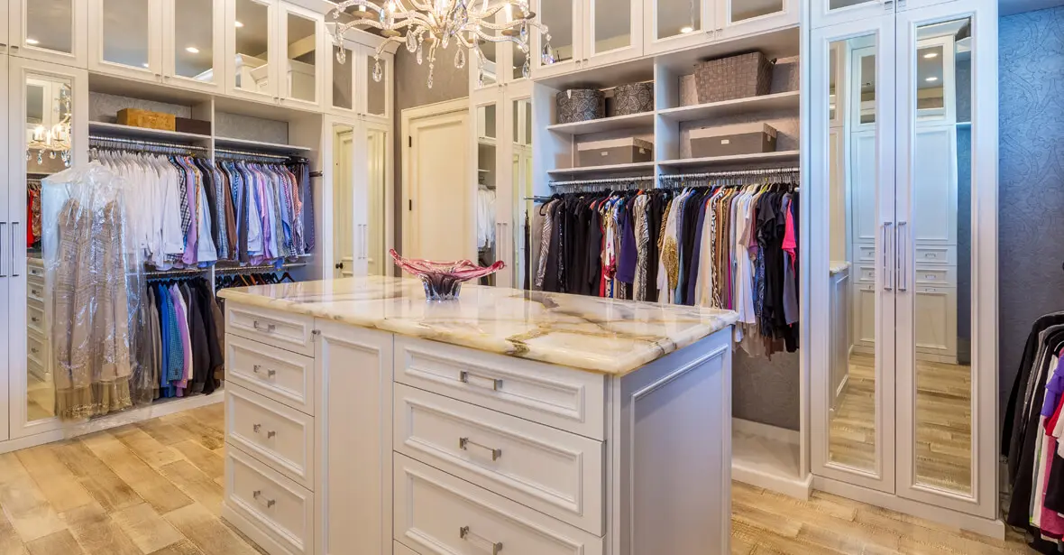 A bright modular walk-in closet with marble island and chandelier.